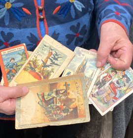 Die Ehrenamtliche Gisela hält Reklame-Sammelbilder und Mini-Bilderbüchlein aus dem 19. Jahrhundert in den Händen.
