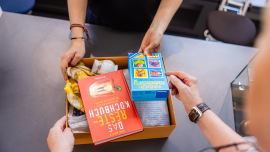 Eine kleine Kiste mit Sachspenden, u.a. einem Kochbuch und einem Spiel, wird im Oxfam Shop abgegeben.