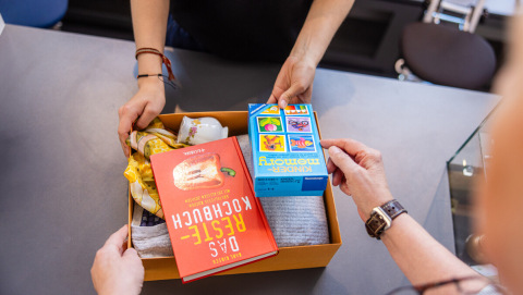 Eine kleine Kiste mit Sachspenden, u.a. einem Kochbuch und einem Spiel, wird im Oxfam Shop abgegeben.