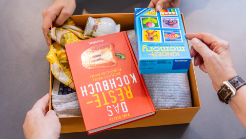 Eine kleine Kiste mit Sachspenden, u.a. einem Kochbuch und einem Spiel, wird im Oxfam Shop abgegeben.